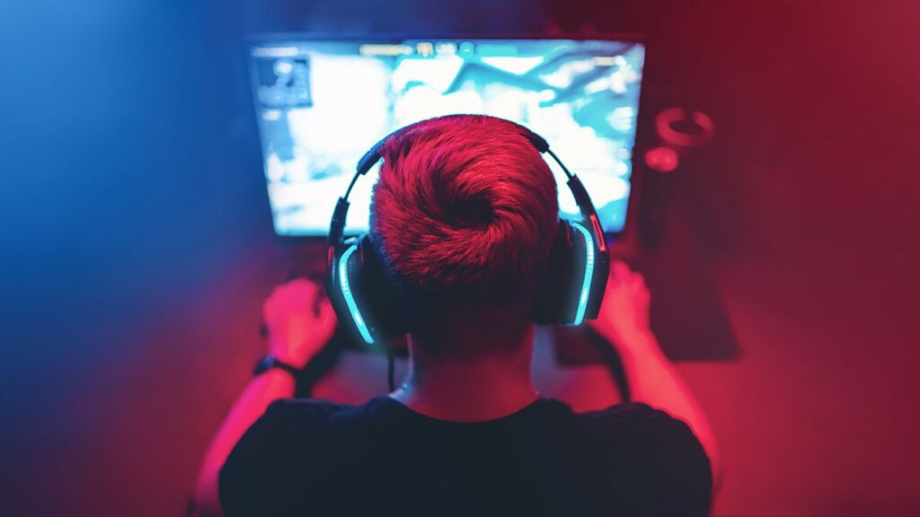 Ragazzo gioca ai videogames davanti a monitor con cuffie