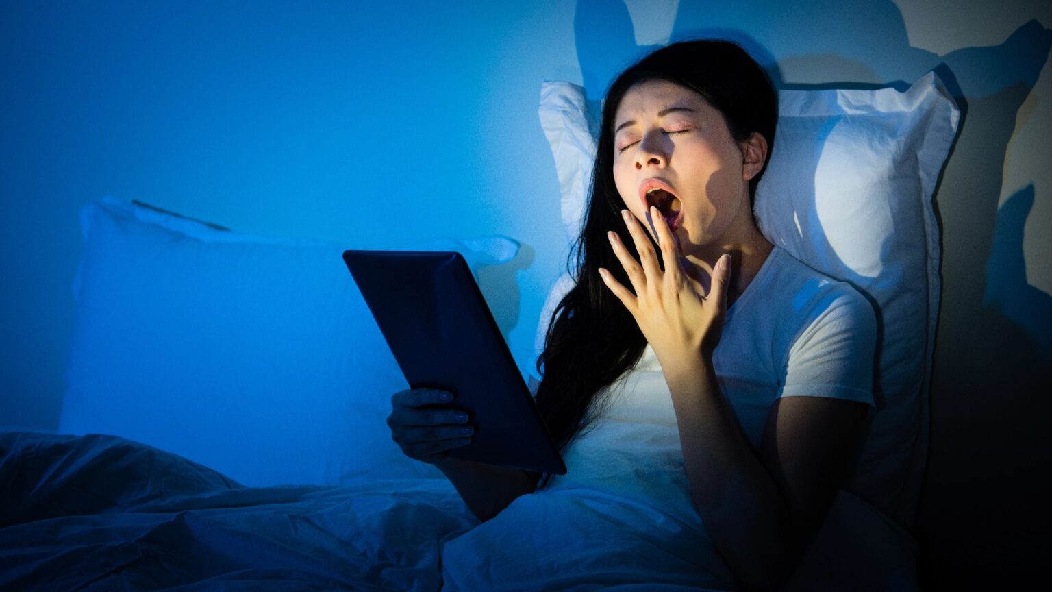 Donna sbadiglia a letto guardando il telefono